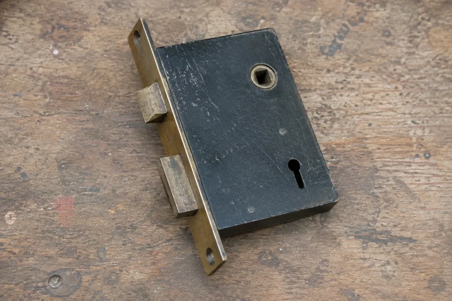 Closed mortise lock case with spindle opening, keyhole, latch and deadbolt on a wooden workbench. — Vintage Mortise Lock Service, Toronto